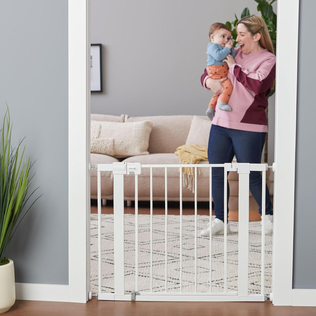 Woman holding a child next to a white baby gate in a living room.